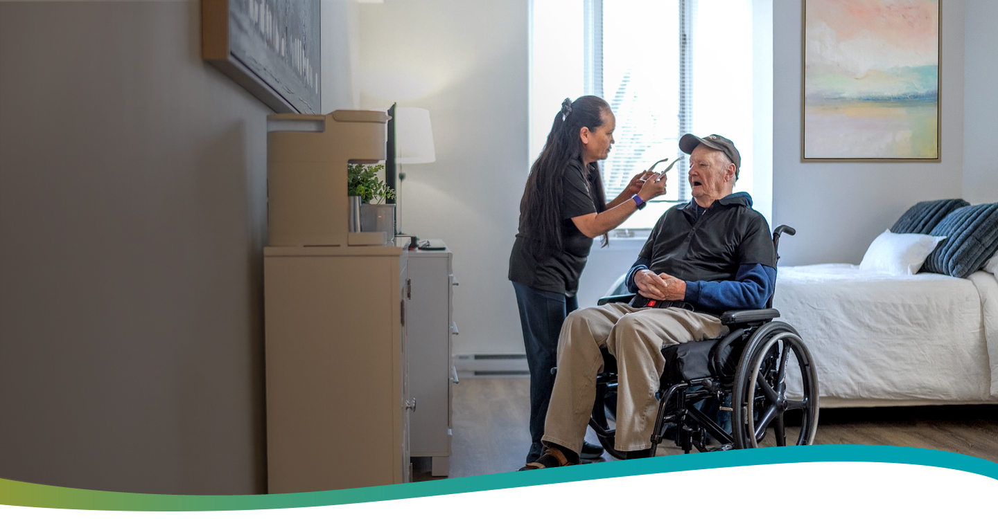 Caregiver helping a resident put on his sunglasses in a suite at Atrium Retirement Residence in Orillia.